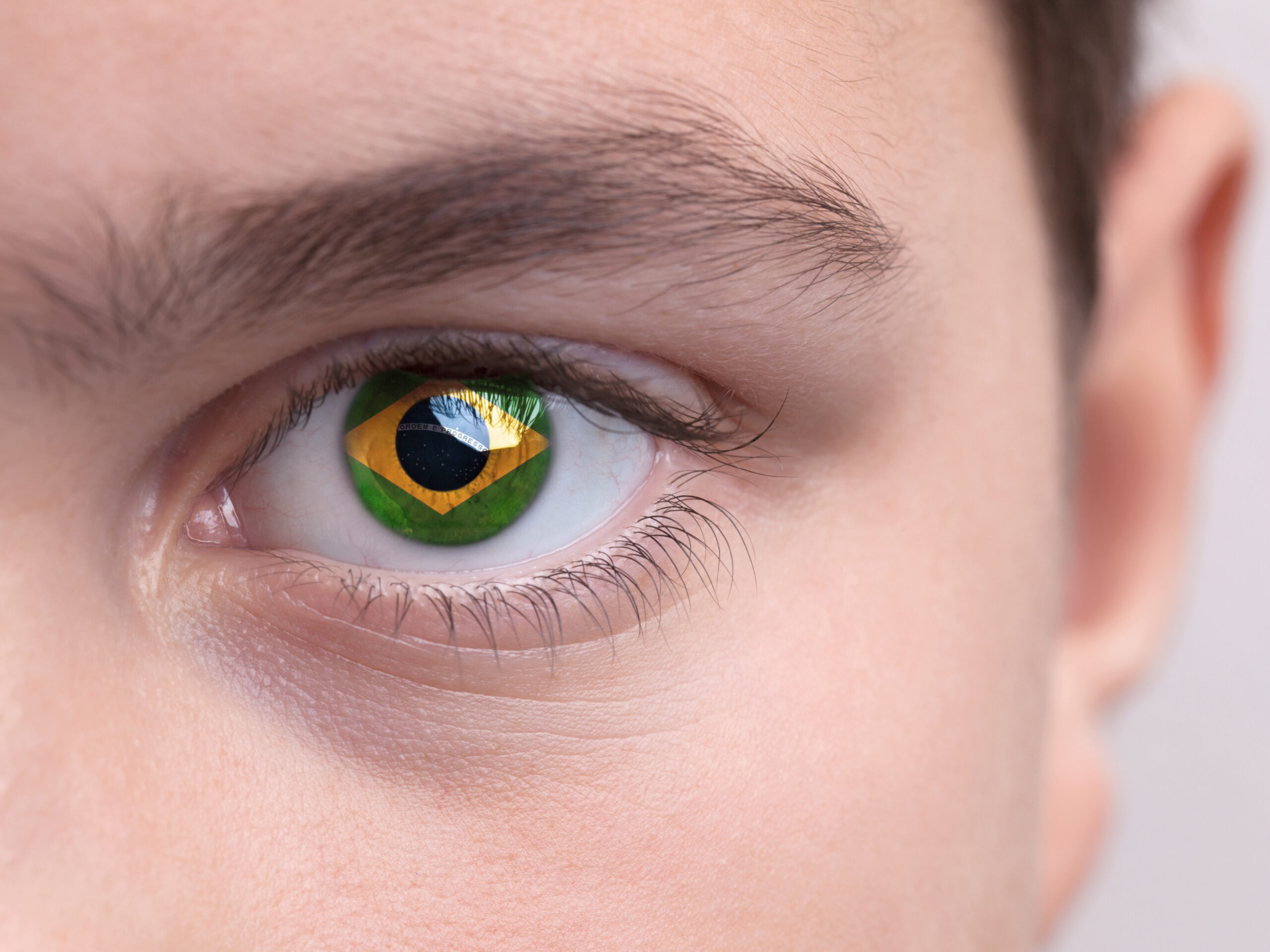 a foto mostra um pedaço do rosto de um homem, aparece somente um olho em que se vê na íris a bandeira do brasil